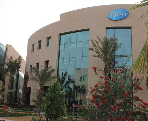 The Business Gate features a contemporary curved design with large glass windows, framed by palm trees and landscaped gardens, offering a distinguished corporate setting.